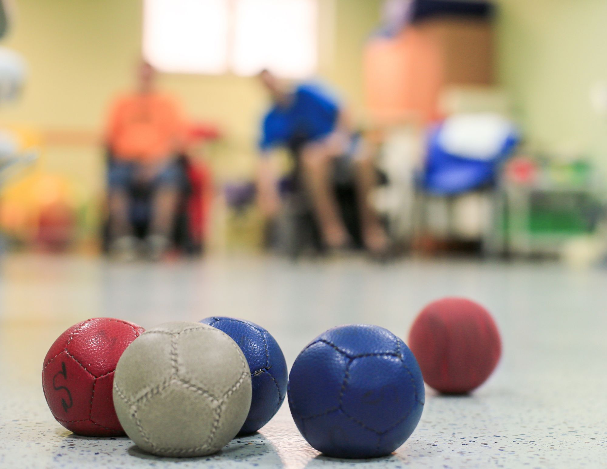 Photo avec des balles bleues, rouges et blanches en avant-plan avec deux hommes en chaise roulante en arrière-plan